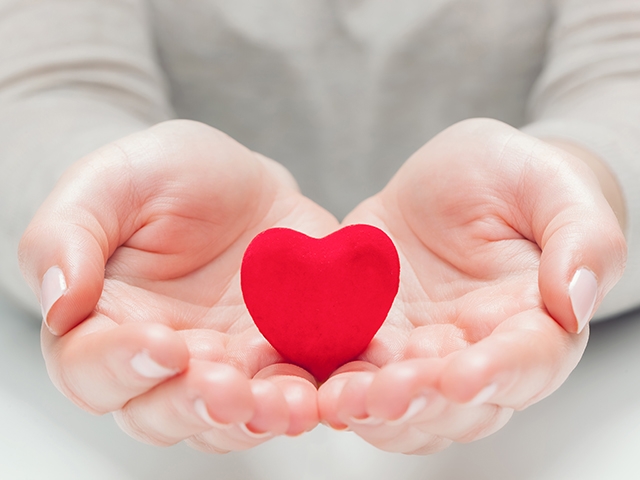 Small red heart in woman's hands in a gesture of giving, protecting. Health, life, love symbol.